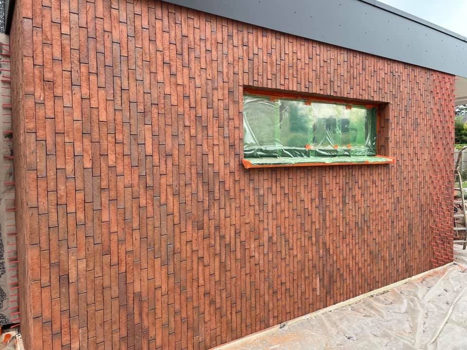 Detail van roodbruine steenstrips voegloos geplaatst rond een raamopening